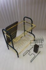 Two-tier gold and black metal dish drying rack with removable drip tray and utensil holder on a white marble kitchen countertop.