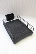 Matte black metal dish drying rack with attached utensil holder and drip tray sitting on a marble kitchen countertop beside a sink.