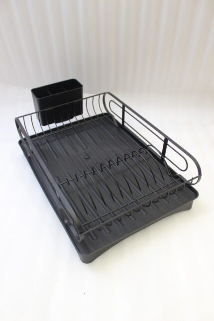 Matte black metal dish drying rack with attached utensil holder and drip tray sitting on a marble kitchen countertop beside a sink.