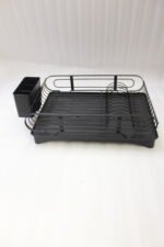 Matte black metal dish drying rack with attached utensil holder and drip tray sitting on a marble kitchen countertop beside a sink.