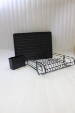 Matte black metal dish drying rack with attached utensil holder and drip tray sitting on a marble kitchen countertop beside a sink.
