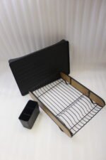 Matte black metal dish drying rack with natural wooden side accents, a black cutlery holder, and a removable drip tray sitting next to a kitchen sink.