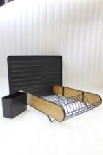 Matte black metal dish drying rack with natural wooden side accents, a black cutlery holder, and a removable drip tray sitting next to a kitchen sink.