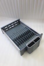 Modern grey and silver expandable kitchen dish drying rack with plate slots, utensil caddy, and drain spout sitting on a countertop next to a sink.