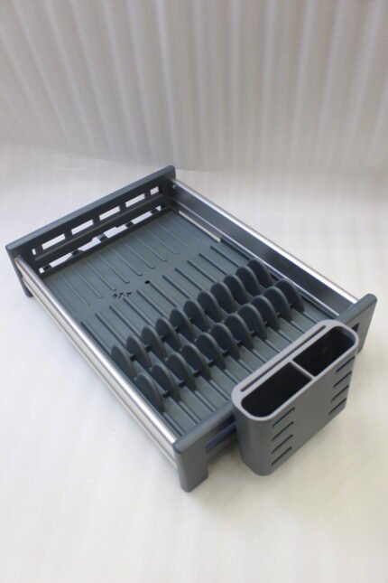 Modern grey and silver expandable kitchen dish drying rack with plate slots, utensil caddy, and drain spout sitting on a countertop next to a sink.