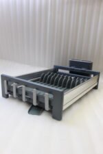 Modern grey and silver expandable kitchen dish drying rack with plate slots, utensil caddy, and drain spout sitting on a countertop next to a sink.