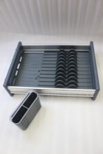 Modern grey and silver expandable kitchen dish drying rack with plate slots, utensil caddy, and drain spout sitting on a countertop next to a sink.