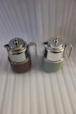 Two One More 1 Liter thermal vacuum coffee carafes in brown and sage green with ribbed bases and polished stainless steel tops on a kitchen counter.