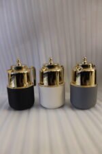 Three One More 1 liter luxury thermal vacuum flasks in black, white, and grey with polished gold tops on a marble kitchen countertop.