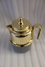 Three One More 1 liter luxury thermal vacuum flasks in black, white, and grey with polished gold tops on a marble kitchen countertop.