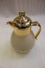 Three luxury 1-liter thermal coffee and tea vacuum flasks with ornate gold lids and accents in matte black, cream, and taupe on a granite kitchen countertop.