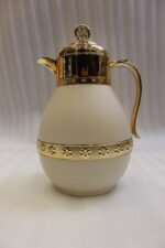 Three luxury 1-liter thermal coffee and tea vacuum flasks with ornate gold lids and accents in matte black, cream, and taupe on a granite kitchen countertop.Three luxury 1-liter thermal coffee and tea vacuum flasks with ornate gold lids and accents in matte black, cream, and taupe on a granite kitchen countertop.